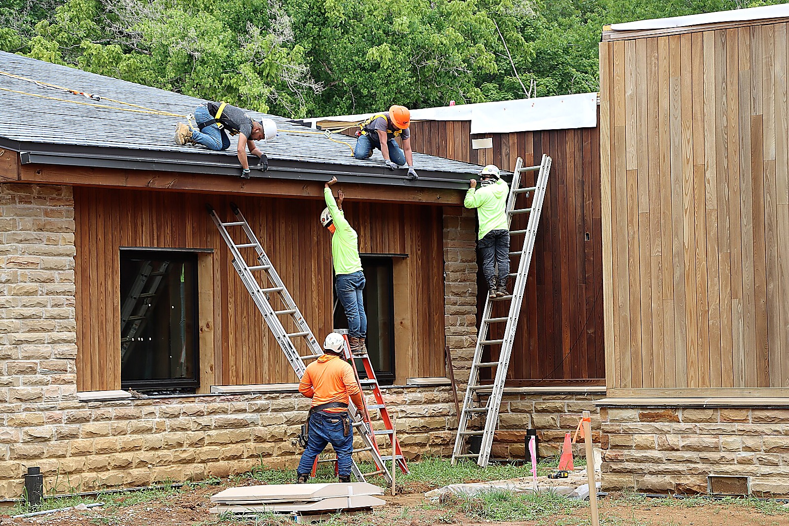 Two workers on ladders fitting a new gutter along a roofline