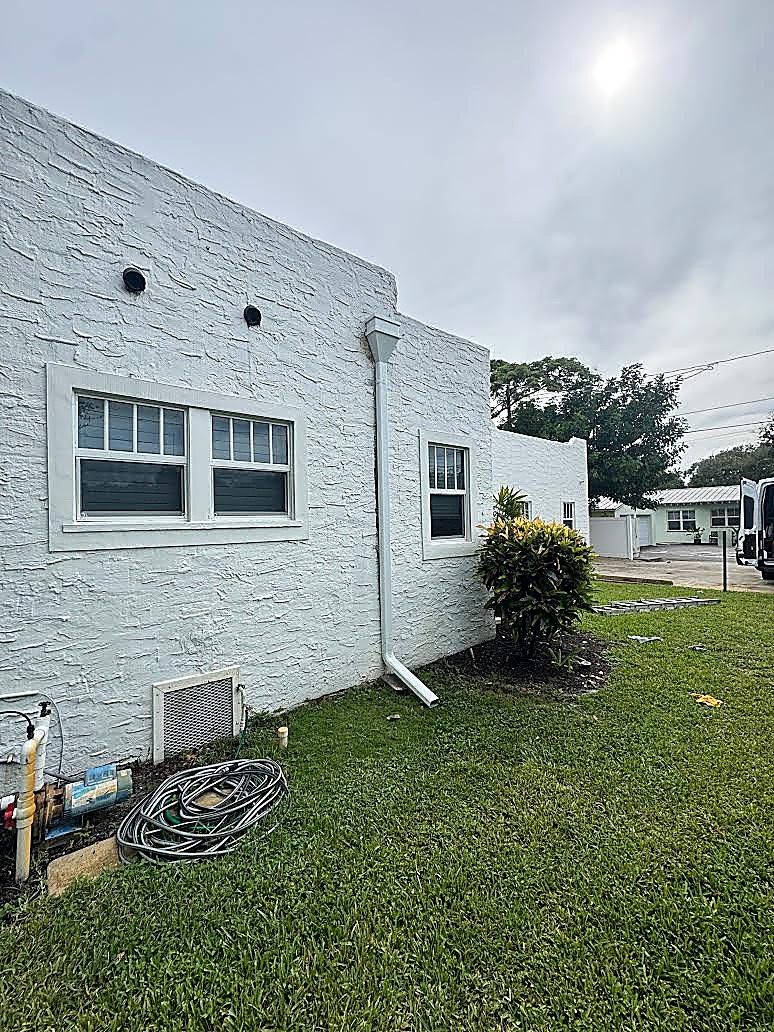 New white downspout running down a white stucco wall