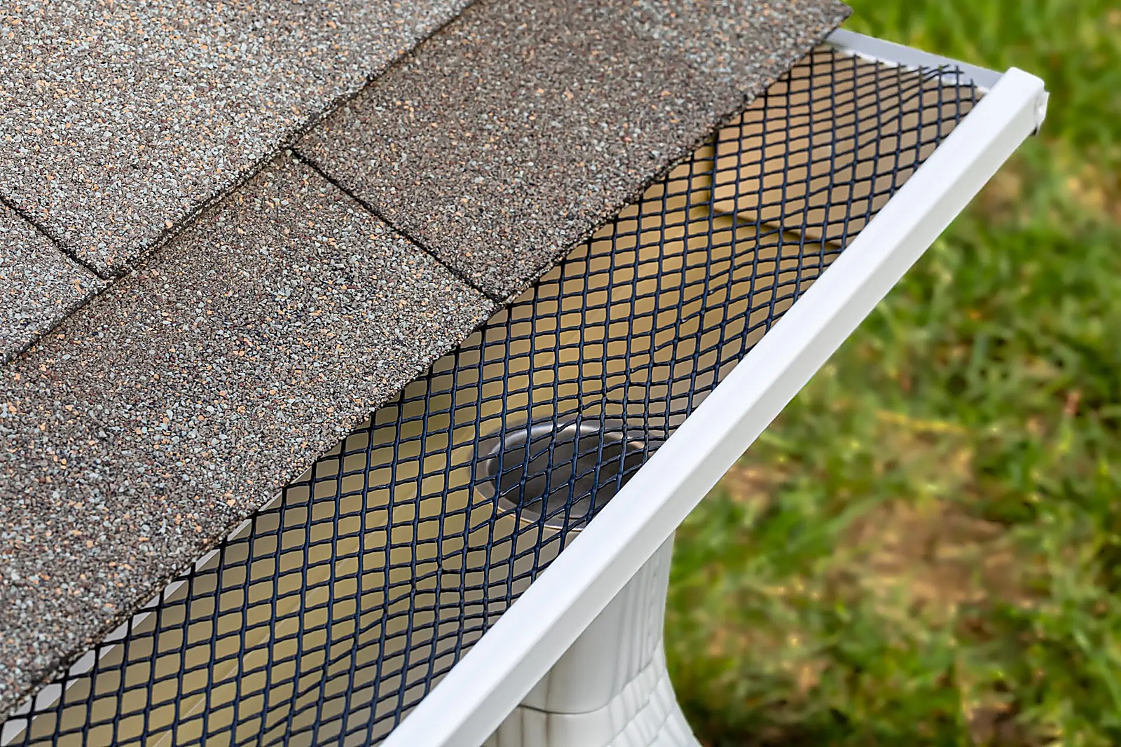 Black mesh leaf guard on a white gutter under asphalt shingles