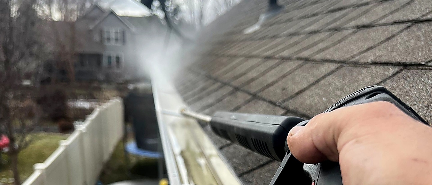Professional pressure-cleaning a residential rain gutter